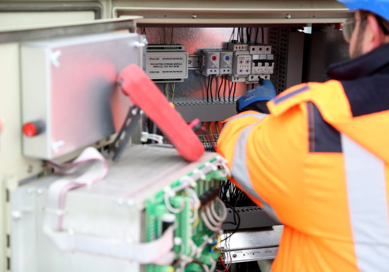 Elektriker in Warnjacke arbeitet an einer Schaltanlage