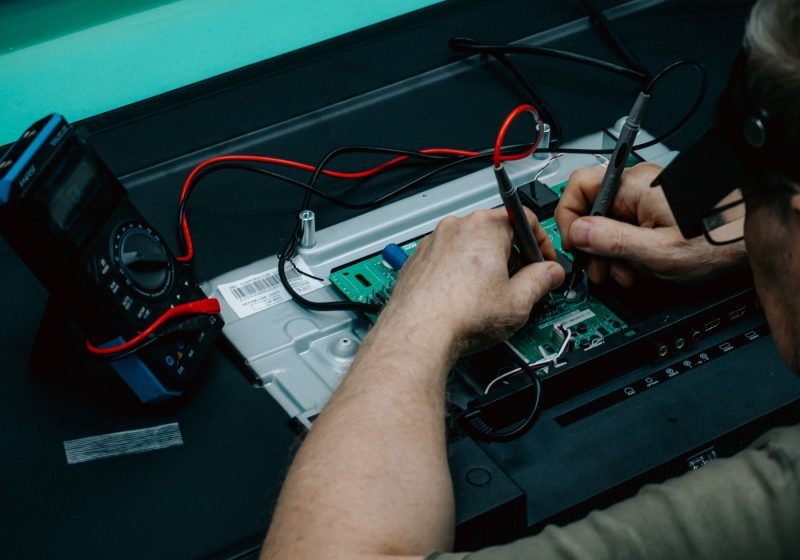 Hände messen mit dem Multimeter an einer Elektronikplatine