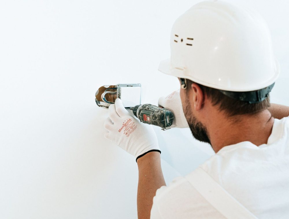Elektriker mit Helm bohrt in eine Wand für eine Installation