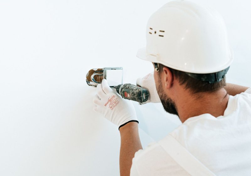Elektriker mit Helm bohrt in eine Wand für eine Installation